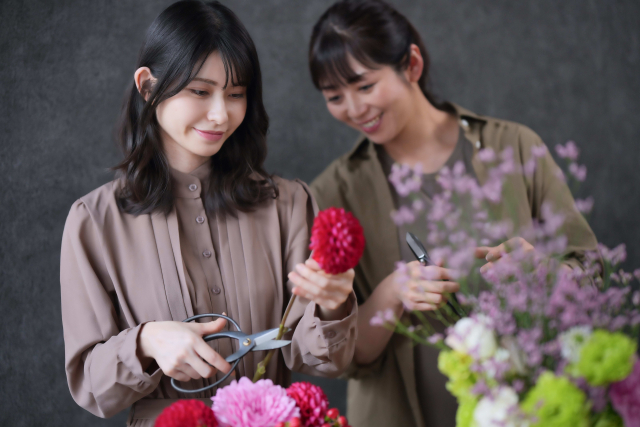 お花教室で楽しそうにフラワーアレンジメントをする女性二人の画像